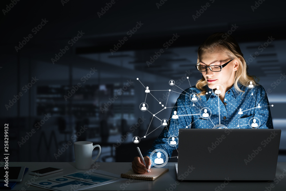 Attractive blonde wearing glasses in dark office using laptop. Mixed media