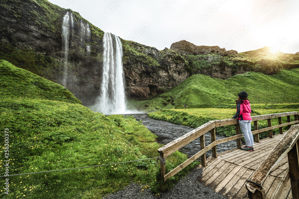 Woman traveler at Magical Seljalandsfoss Waterfall in Iceland located near ring road of South Icelan