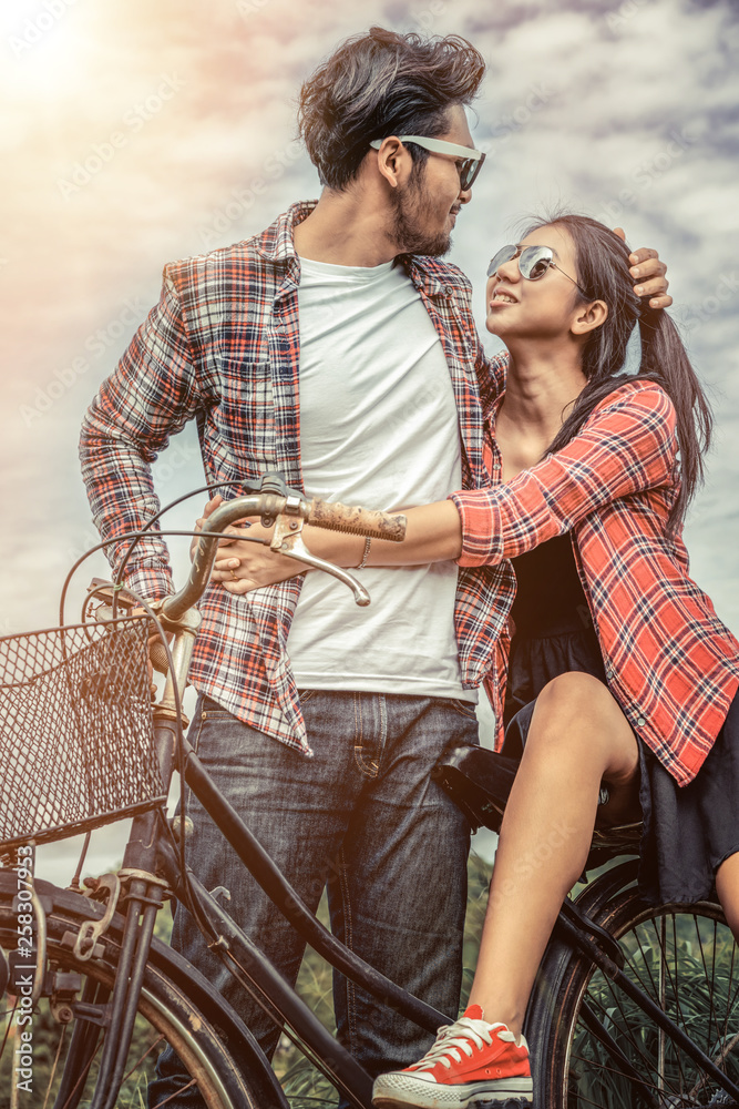 Happy young couple of man and woman ride bicycle at green grass field on the hills. Love and travel 