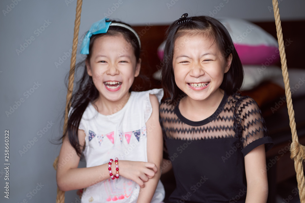 Asian sisters laughed happily sit on inhouse swing set