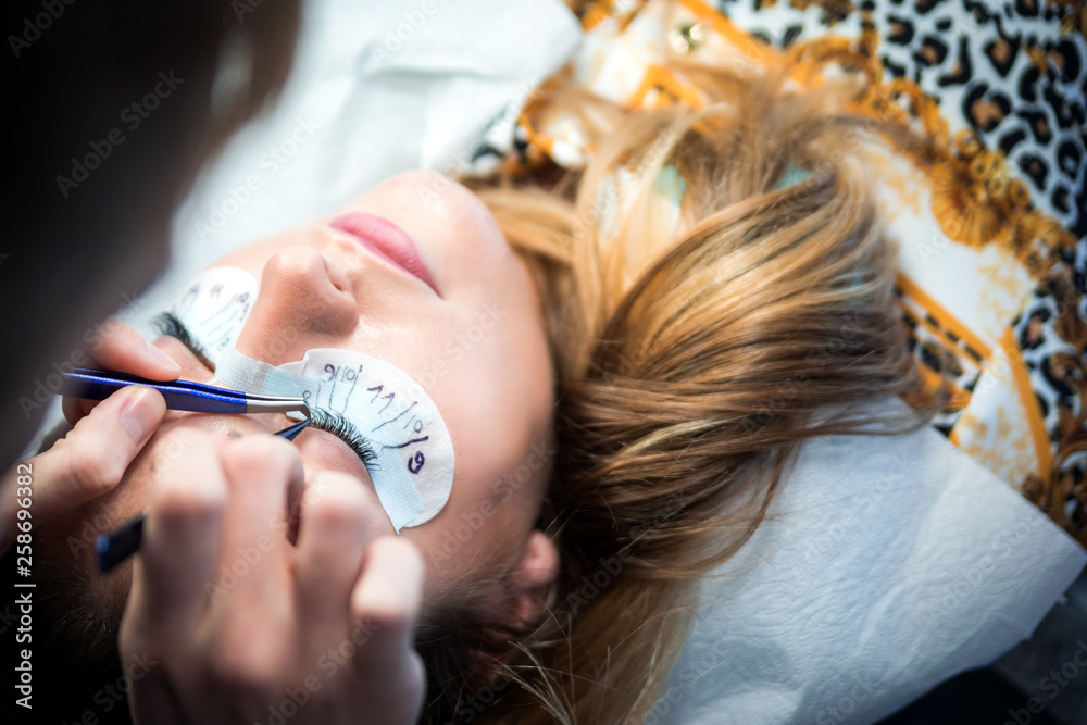 Male beautician applying extension eyelashes at beauty salon