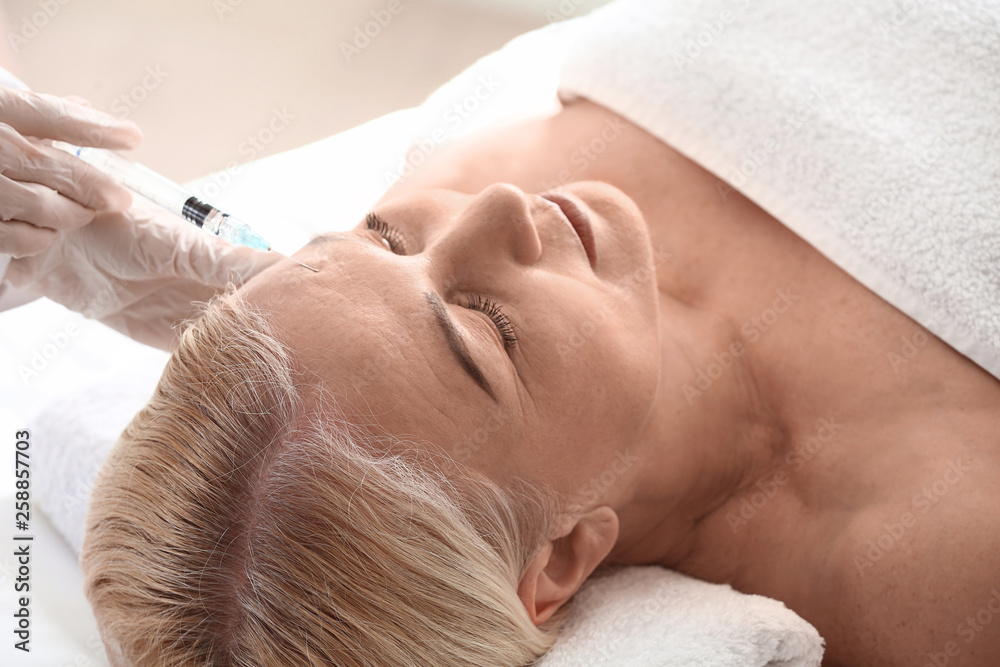 Mature woman receiving filler injection in beauty salon