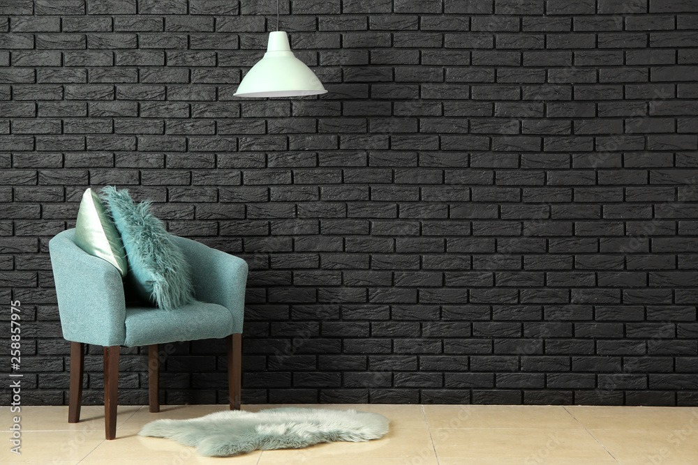 Stylish armchair near dark brick wall