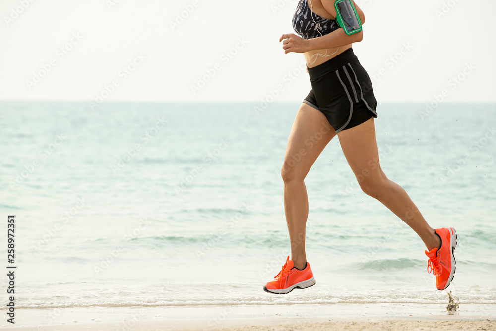 Asia woman in sports bra  listening to music on smartphone armband jogging on the beach. Fitness fem