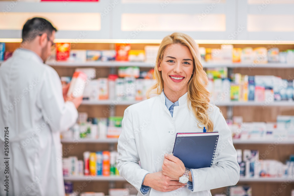 Portrait of a smiling blonde female healthcare worker in a pharmaceutical store, colleague working i