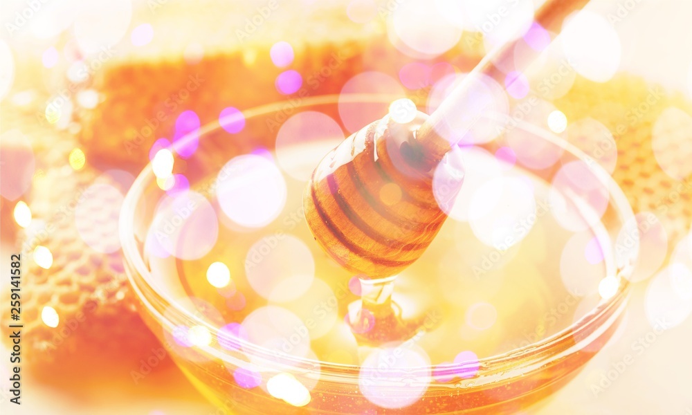 Honey with spoon in glass bowl on glossy background