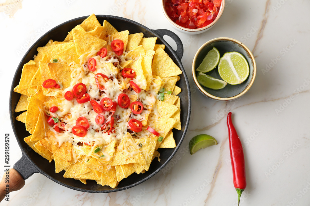 Frying pan with tasty nachos, cheese and chili on light table