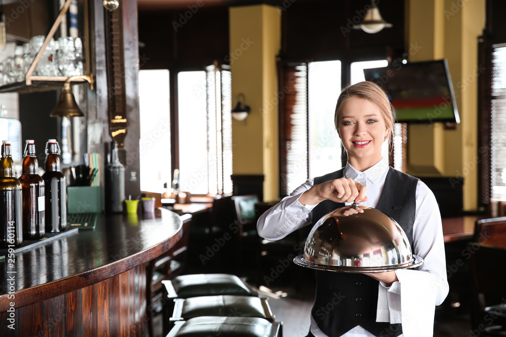 Young female waiter with tray and cloche in restaurant