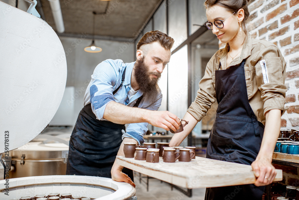 Man and woman taking baked ceramics from eleectric oven, working at the pottery manufacturing