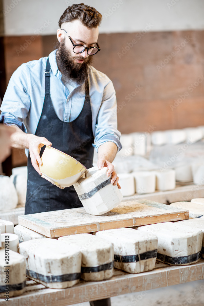 Handsome worker pouring special liquid into the gypsum form at the pottery manufacturing