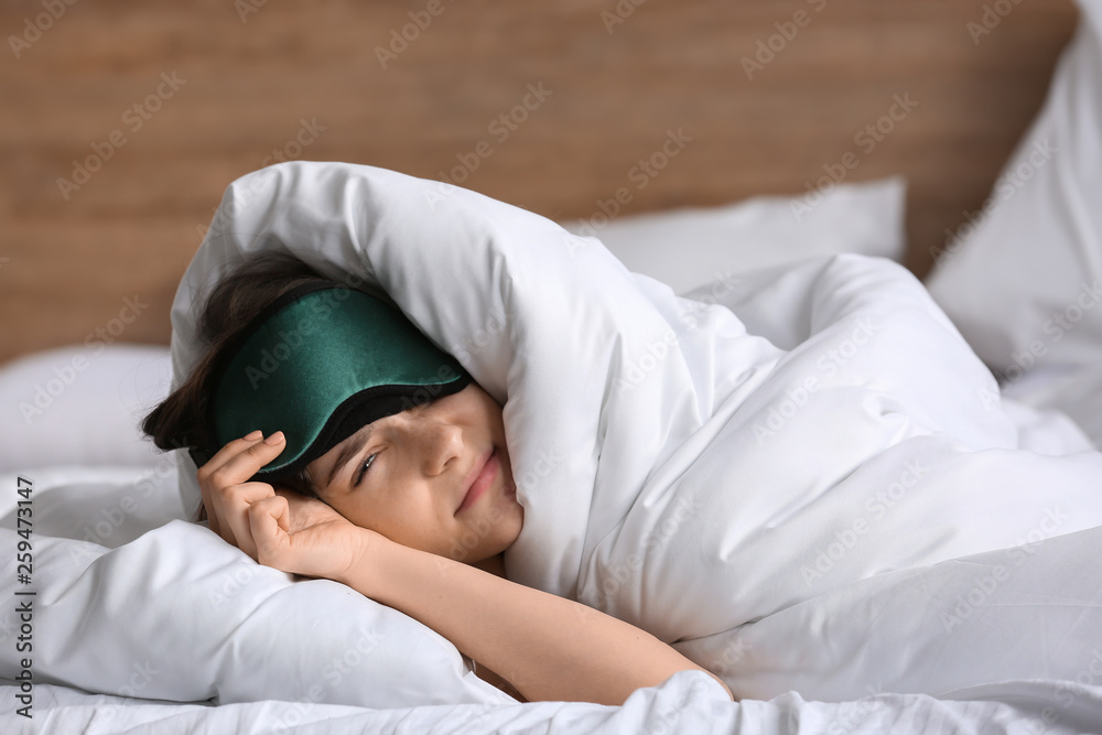 Sleepy young woman with mask in bed