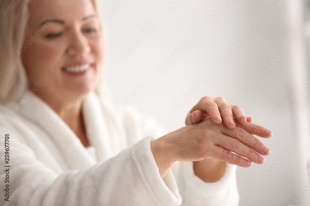 Mature woman applying hand cream at home