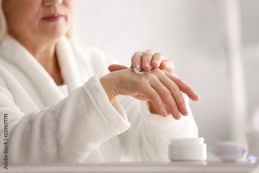 Mature woman applying hand cream at home