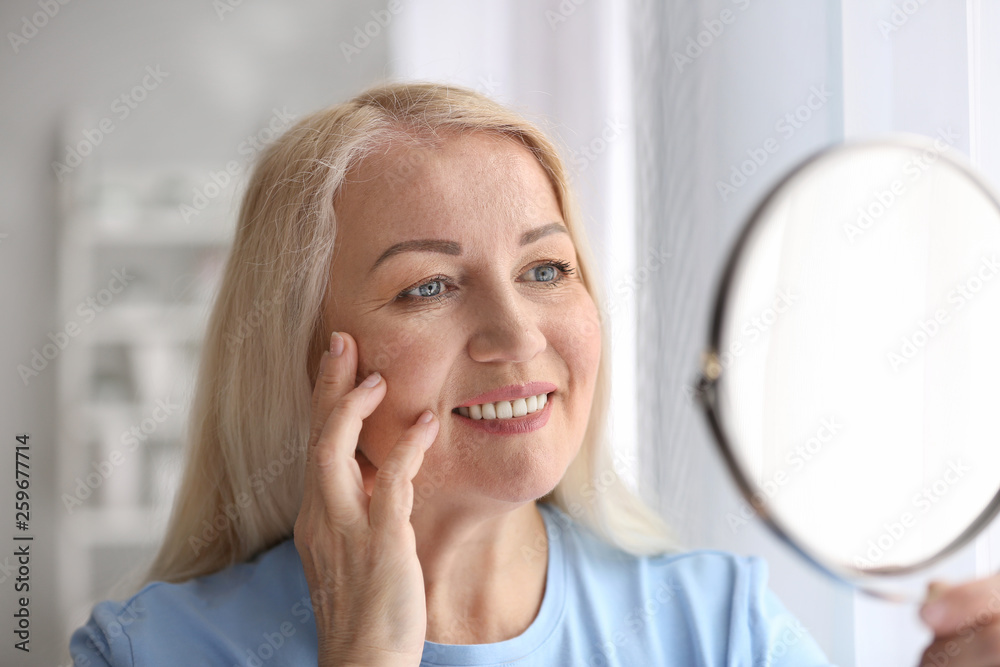 Mature woman with healthy skin looking in mirror at home