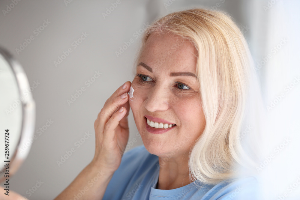 Mature woman applying facial cream at home