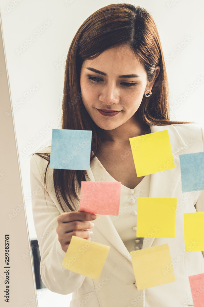 Happy businesswoman thinking creative ideas with sticky notes on glass wall at the office. Work plan