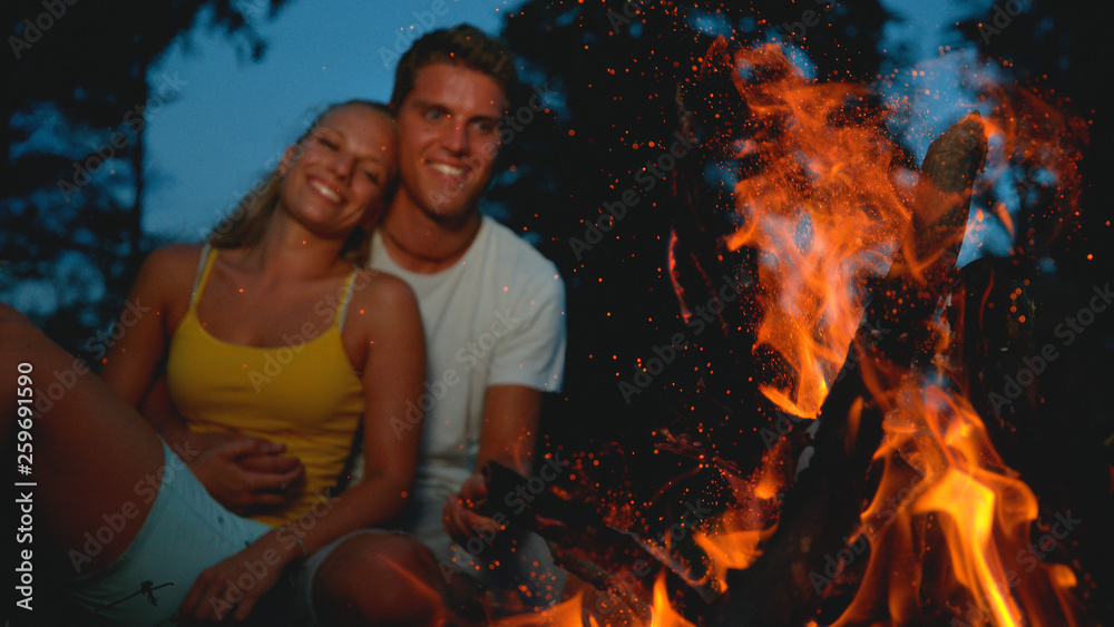 CLOSE UP, DOF: Young couple cuddling and looking at the big burning campfire.