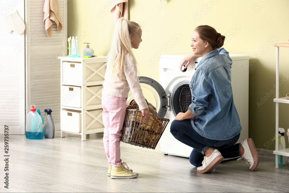 Young woman and her little daughter doing laundry at home