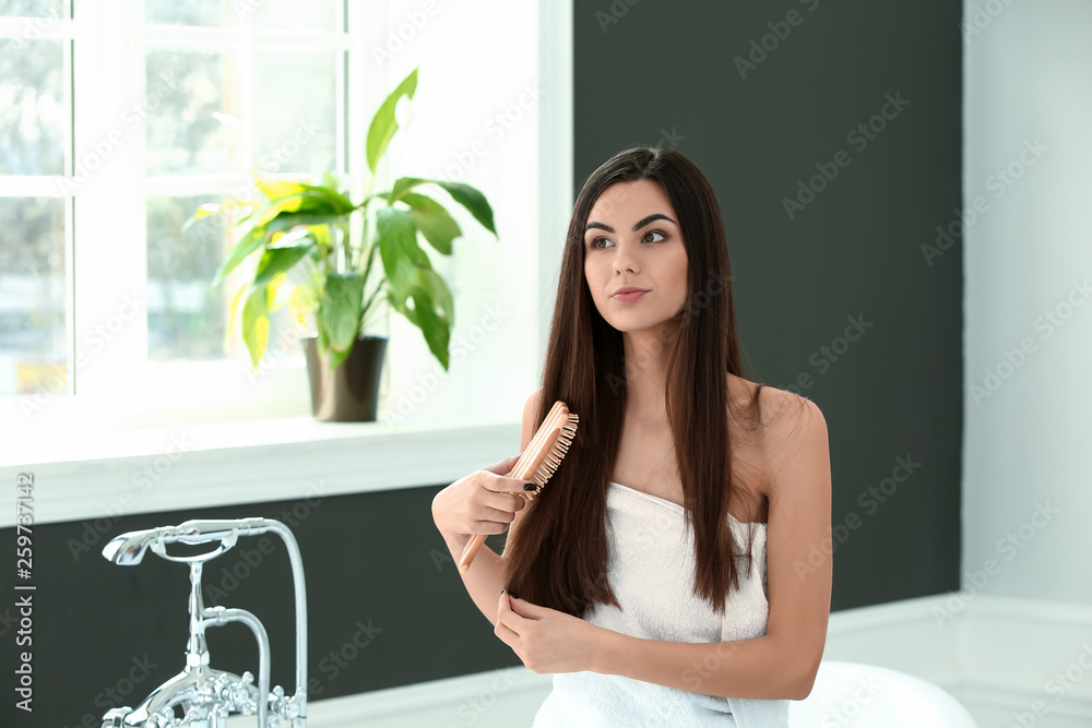 Beautiful young woman brushing her healthy long hair in bathroom