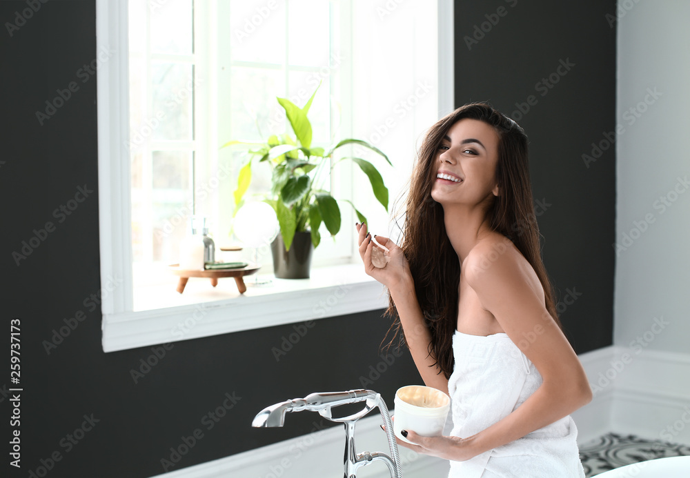 Beautiful young woman applying cosmetics onto her healthy long hair at home