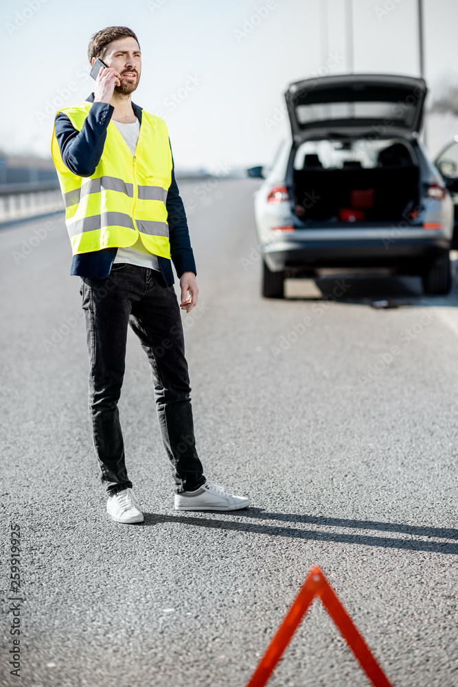 一名身穿背心的男子站在高速公路上破碎的汽车附近呼叫道路救援