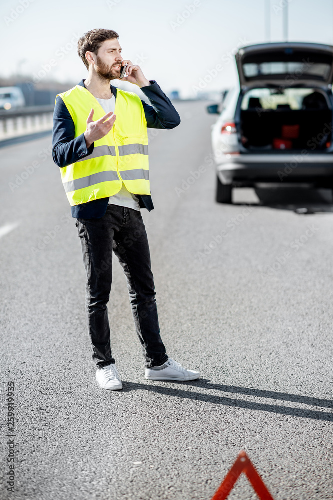 一名身穿背心的男子站在高速公路上破碎的汽车附近呼叫道路救援