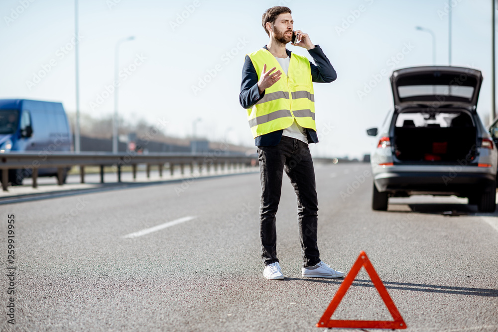 一名身穿背心的男子站在高速公路上破碎的汽车附近呼叫道路救援