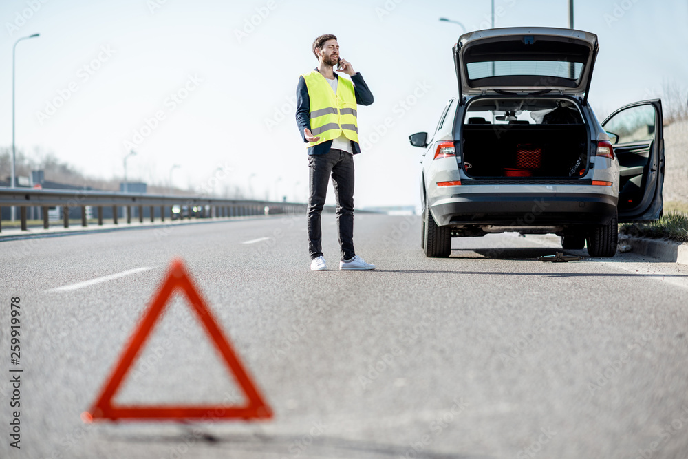 一名身穿背心的男子站在高速公路上破碎的汽车附近呼叫道路救援