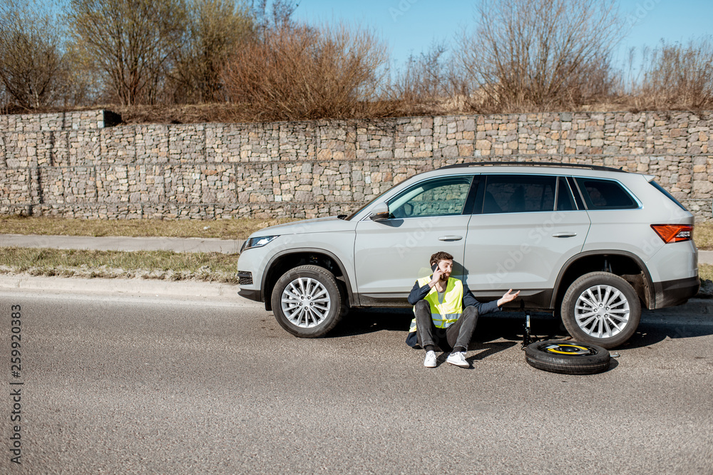 Man sitting near the car on the roadside, wide view