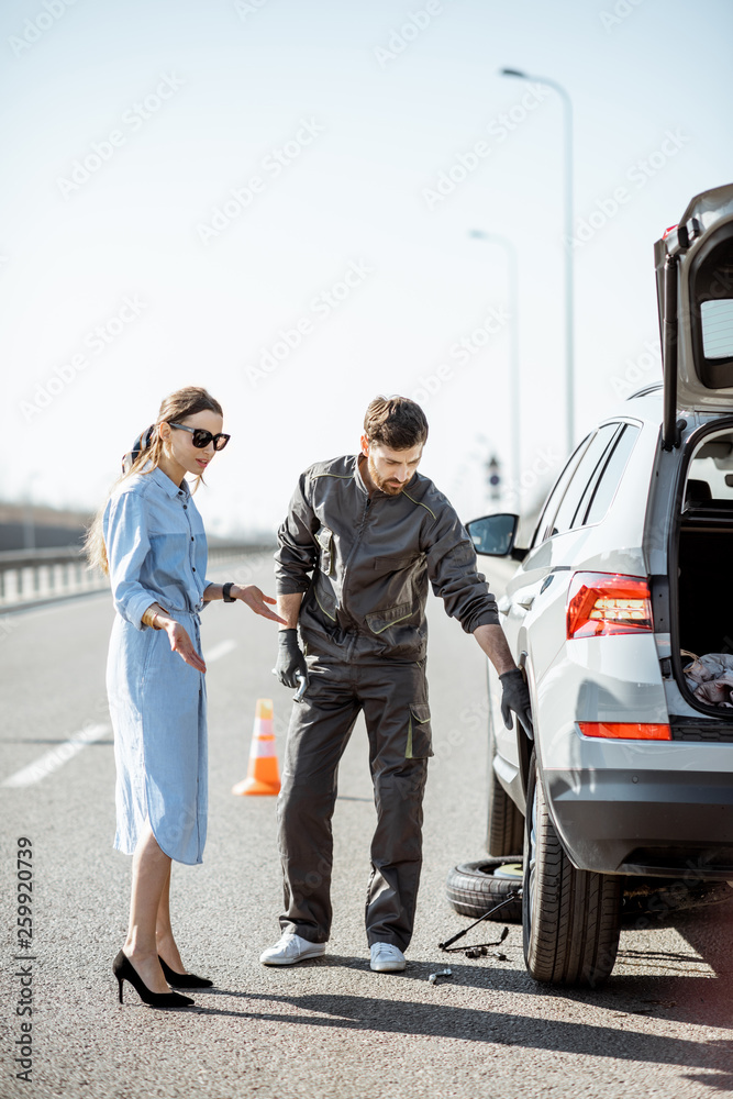 身穿制服的道路救援人员和年轻女子站在高速公路上破碎的汽车附近