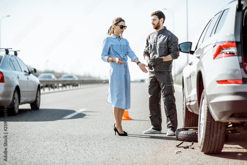 穿着制服的道路救援人员和年轻女子站在高速公路上破碎的汽车附近