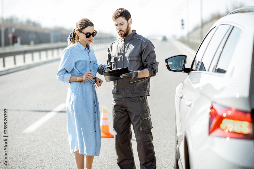 道路救援人员在高速公路上与一名靠近破碎汽车的女子签署了一些文件