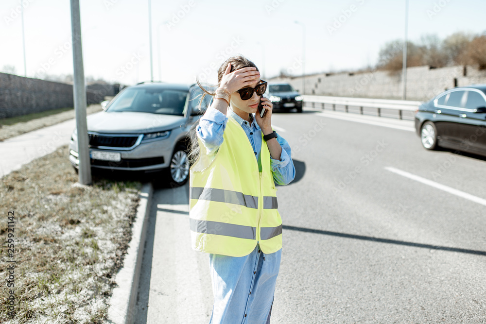 在高处发生道路事故时，一名尴尬的女子站在汽车附近呼叫道路救援