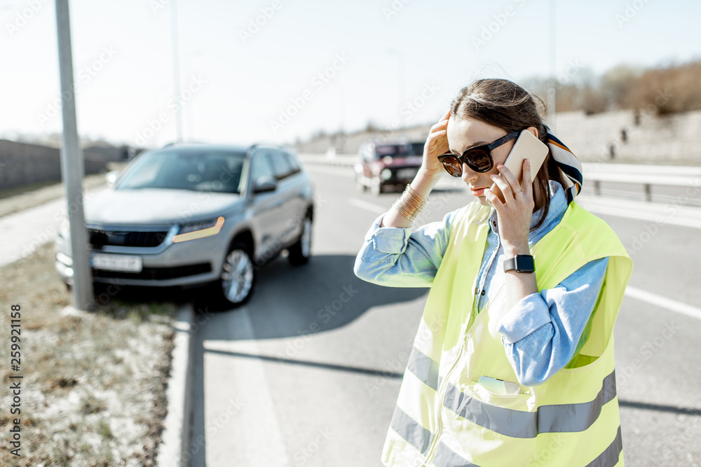 在高处发生道路事故时，一名尴尬的女子站在汽车附近呼叫道路救援