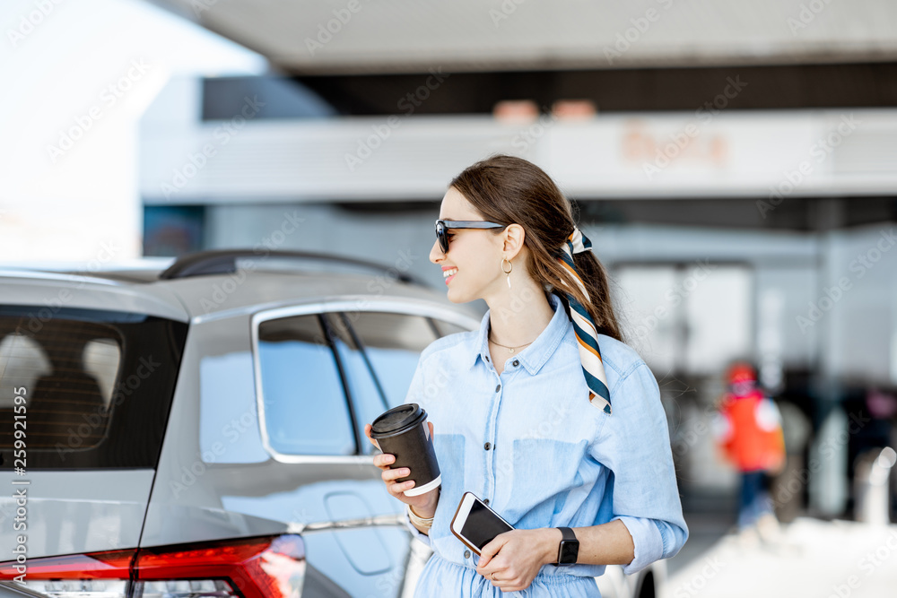 Young woman having a coffee break standing near the car on the gas station