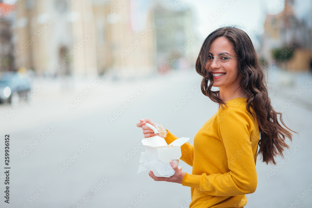 一个微笑的女人拿着外卖走在城市街道上的肖像。