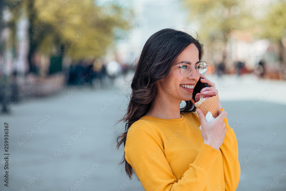 休闲的年轻深色皮肤女人在户外吃冰淇淋和打电话。