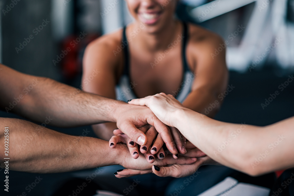 Close-up of sports team stacking hands while sitting in the gym.