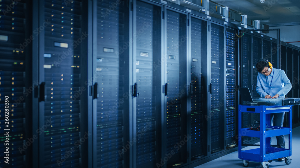 In the Modern Data Center: IT Technician Wearing Protective Headphones Working with Server Racks, on