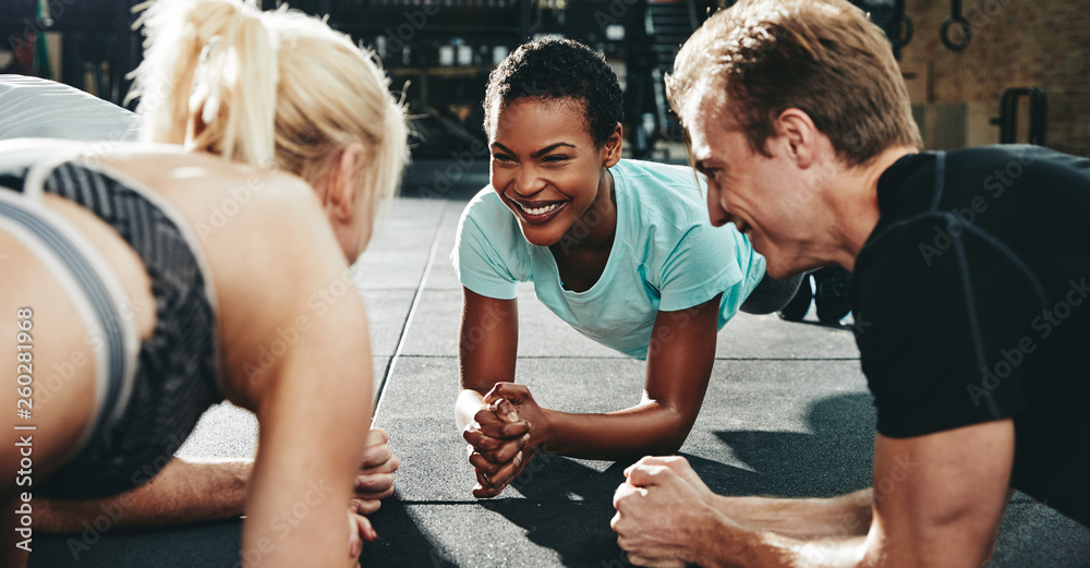 Smiling friends planking together during a gym workout class