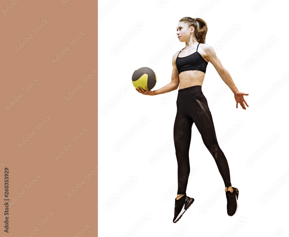 Full length portrait of a female in black sportswear and trainers jumping with a ball in her hand. S