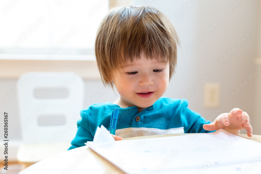 Happy toddler boy drawing at his desk