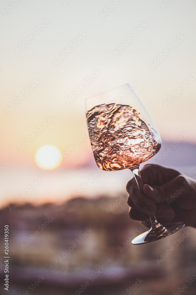 Glass of rose wine in mans hand with sea view and beautiful sunset at background, close-up. Summer e