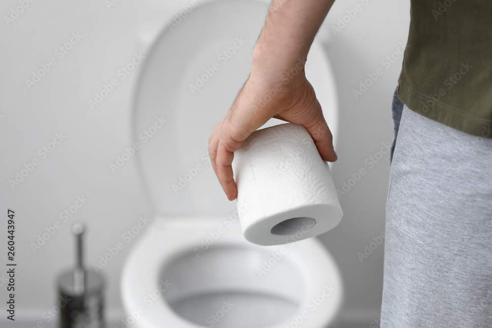 Man with roll of toilet paper in WC, closeup