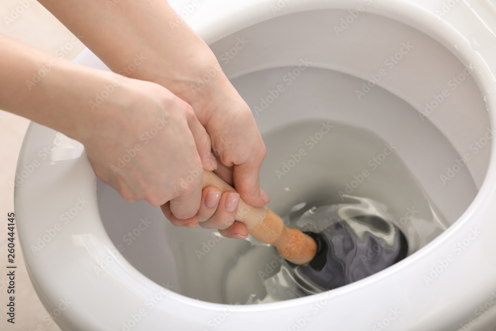 Young woman using plunger to unclog a toilet bowl