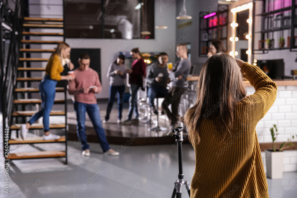 Woman taking photo of young coworkers during coffee break in cafe