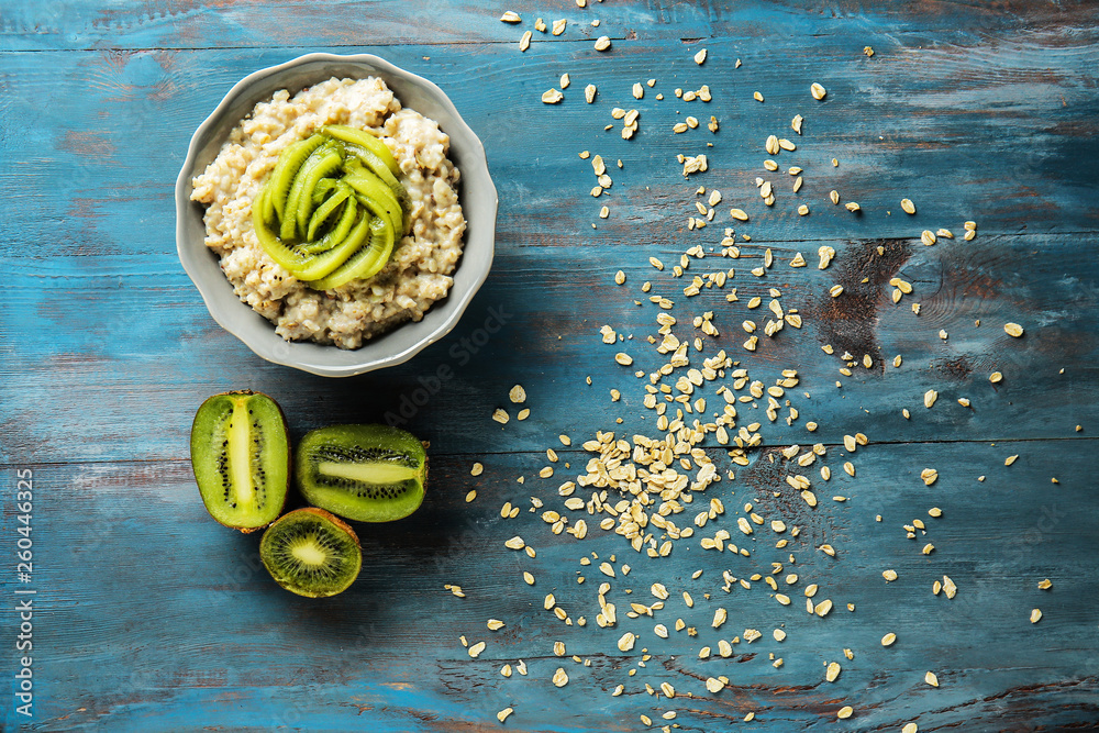 Bowl with tasty sweet oatmeal and kiwi fruit on wooden table