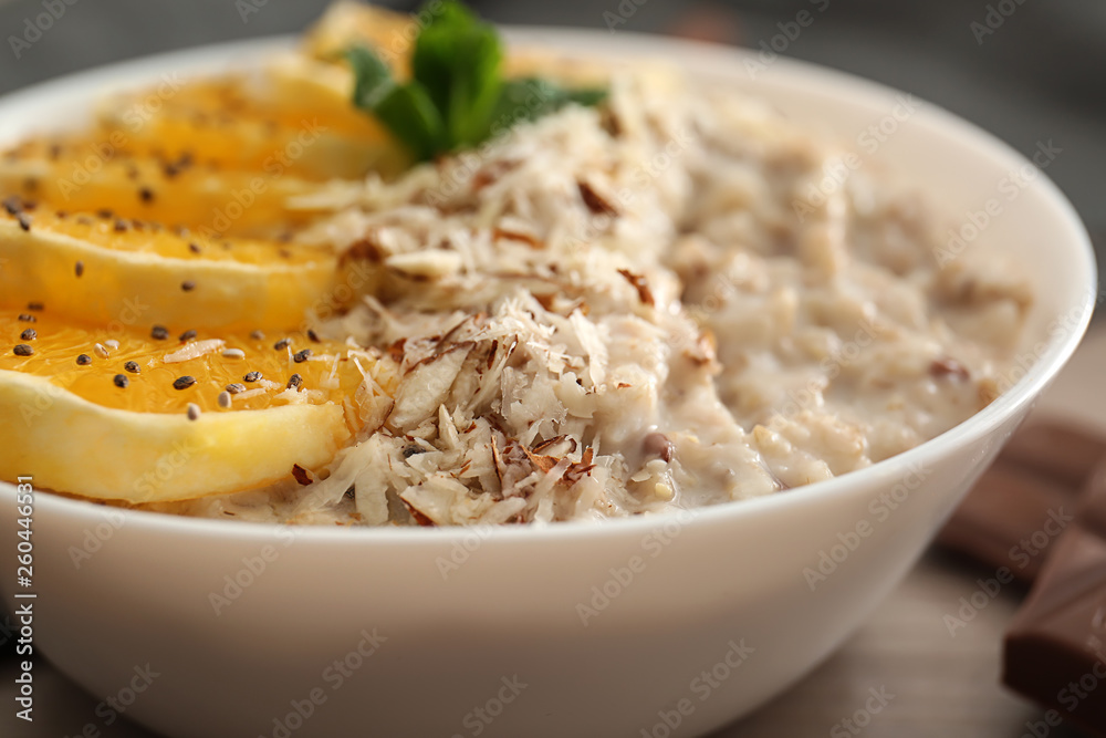 Bowl with tasty sweet oatmeal on table, closeup