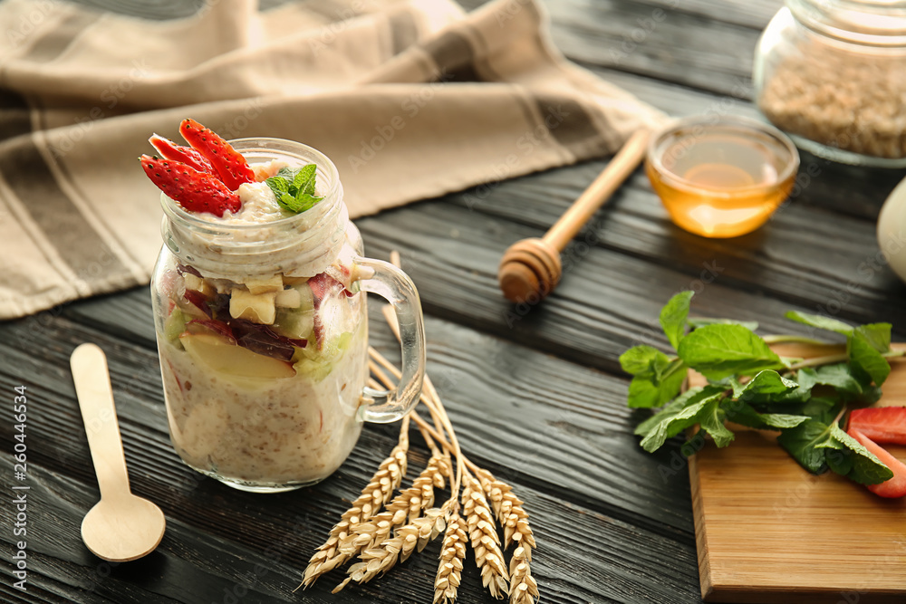 Mason jar with tasty sweet oatmeal on wooden table