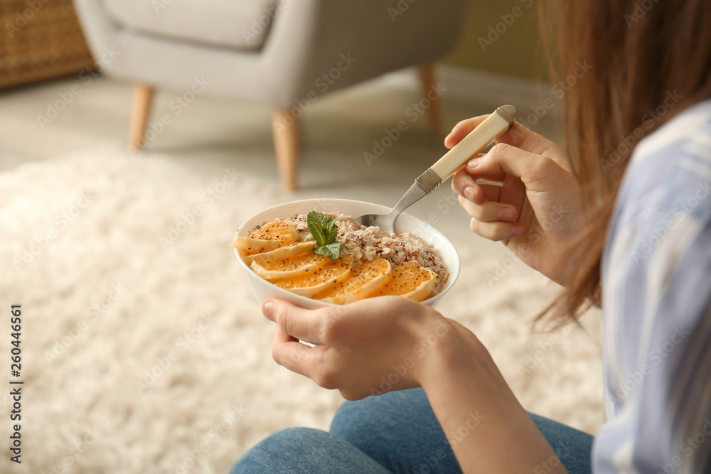 Young woman eating tasty sweet oatmeal at home